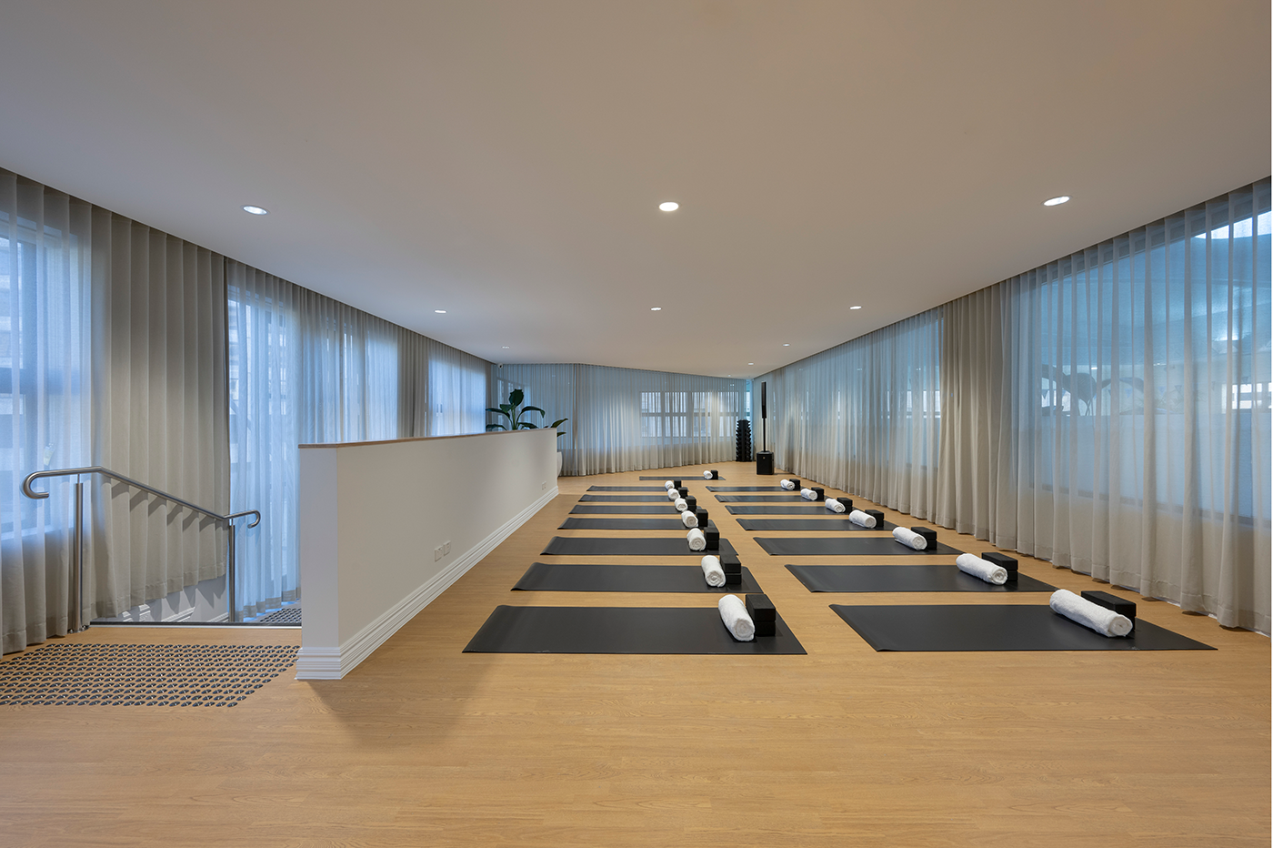 Tattersall's Club. Modern yoga studio with mats, bolsters, and blocks arranged neatly on a wooden floor; large windows with sheer curtains line the walls. Hospitality Interior Design Brisbane Australia
