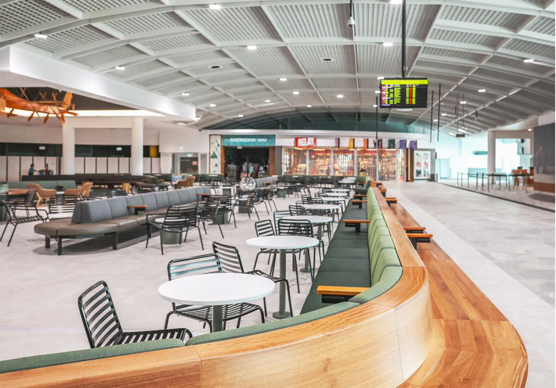 Empty airport lounge with chairs, tables, and an electronic flight information display screen.