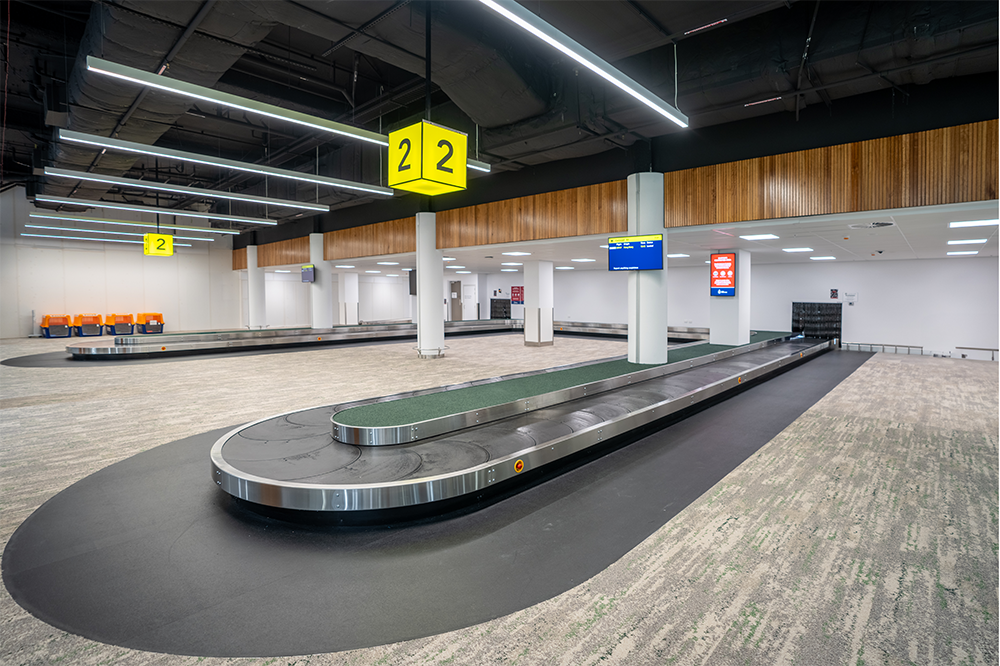 Empty baggage claim area with conveyor belts, digital screens, and yellow signs indicating baggage claim area 2 at an airport.