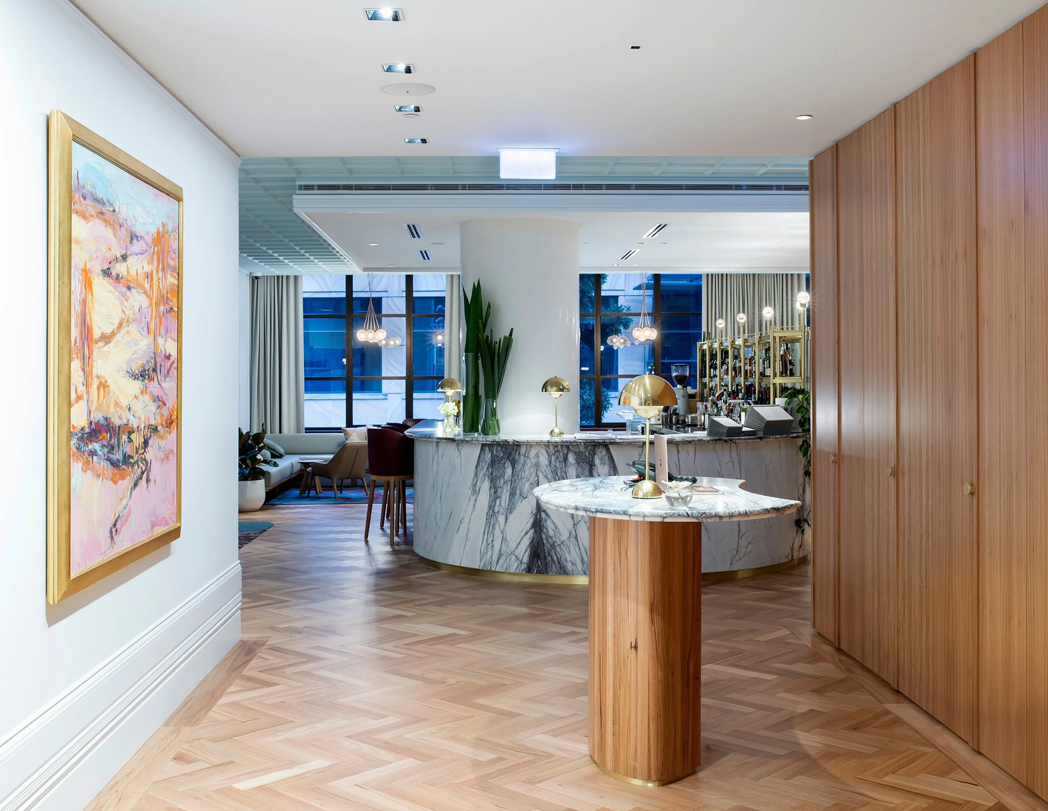 Interior of a modern room with artwork on the wall, a marble counter, tall green plant, and a bar area with bar stools and pendant lights.
