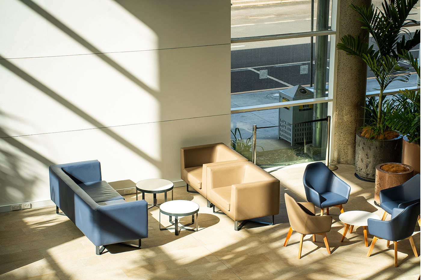 Modern waiting area with blue and beige sofas, armchairs, round tables, large windows, and potted plants. Interior Designers in Brisbane Australia
