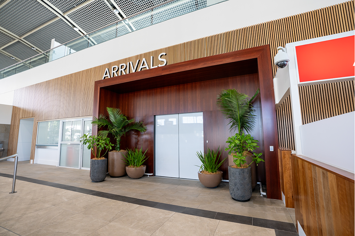 Cairns International T1 Airport. Airport arrivals area with wooden paneling, potted plants, and glass doors. Airport Interior Design Brisbane Australia