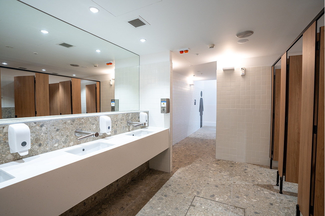 Cairns International T1 Airport. Modern public restroom with sinks, mirrors, soap dispensers, and wooden stall doors. Airport Interior Design Brisbane Australia