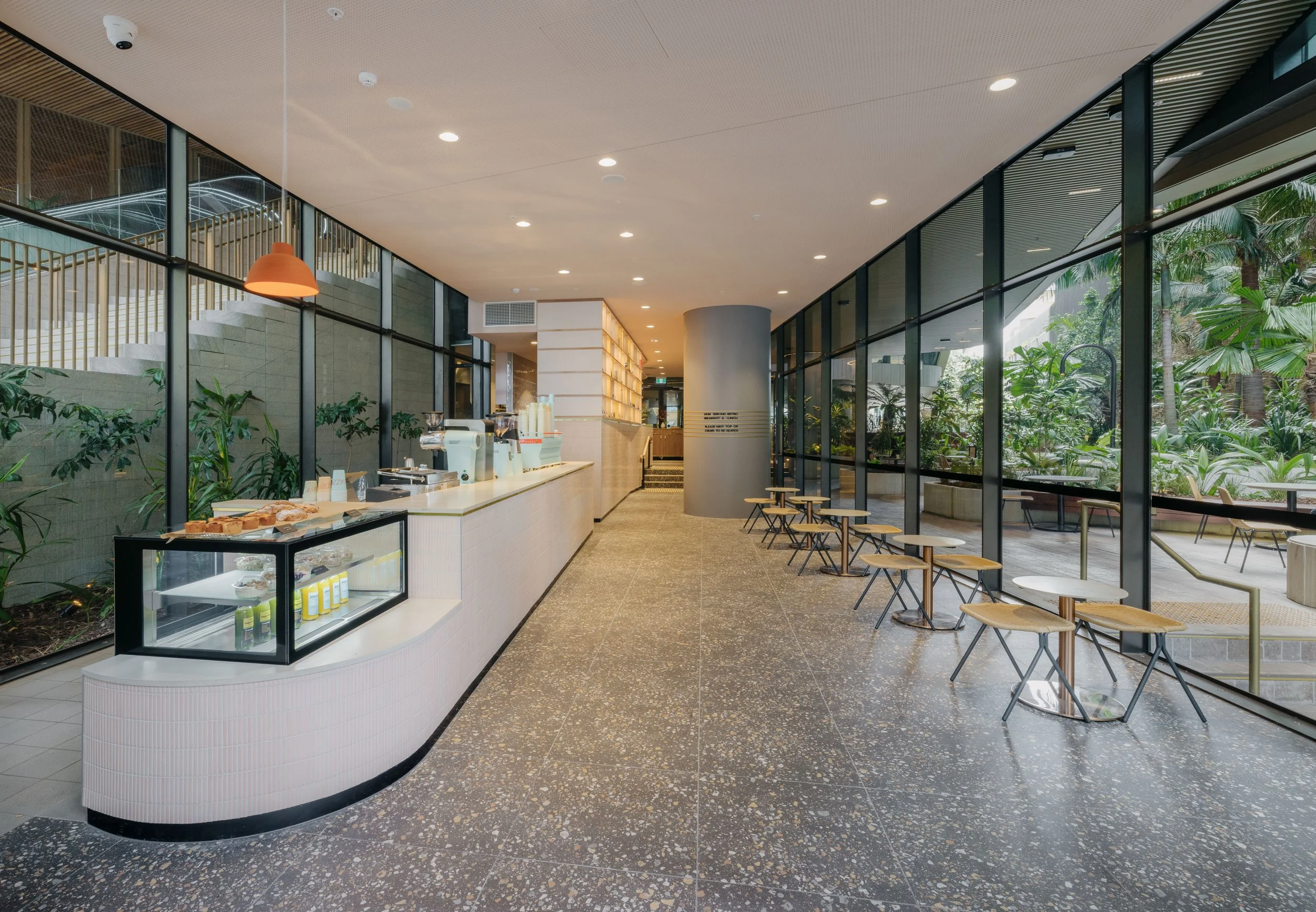 Modern café interior with counter, pastries display, stools, and large windows. Interior Designers in Brisbane Australia