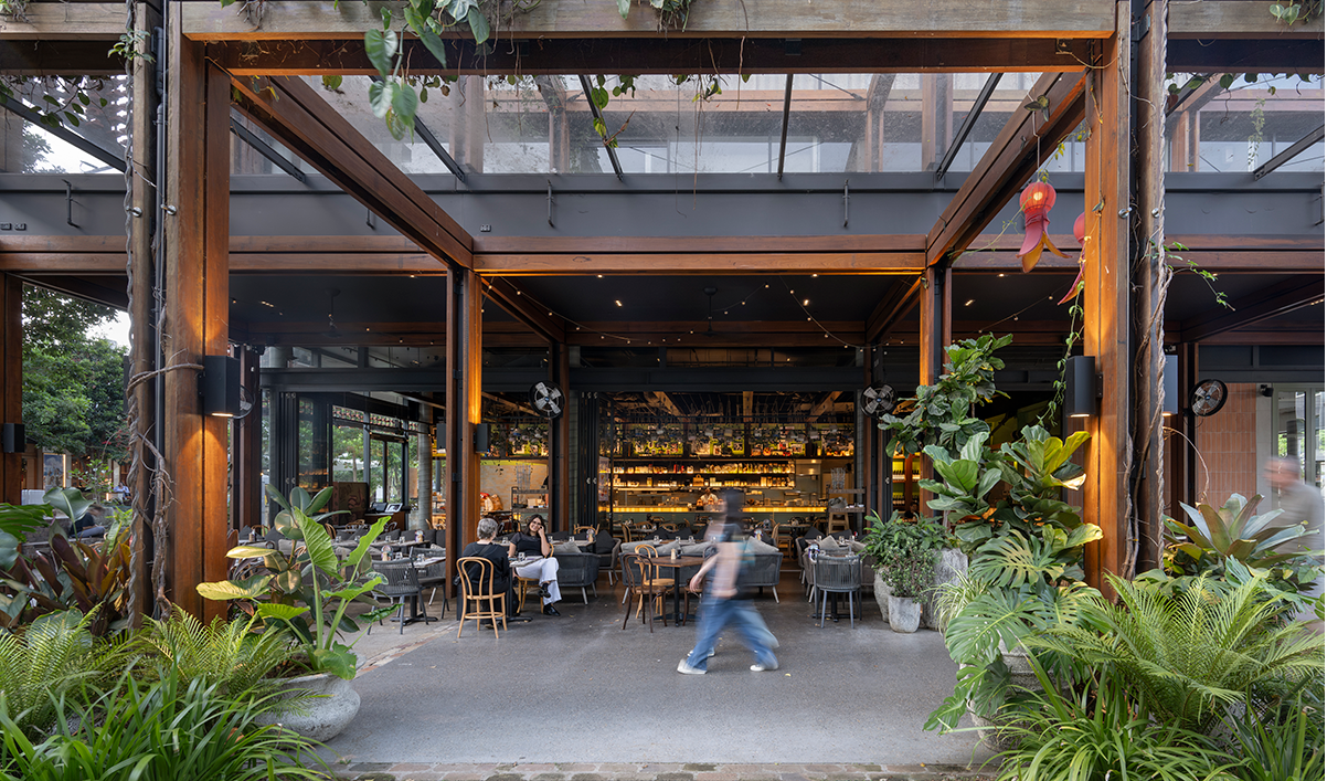 Outdoor restaurant with greenery, wooden beams, and large glass windows.