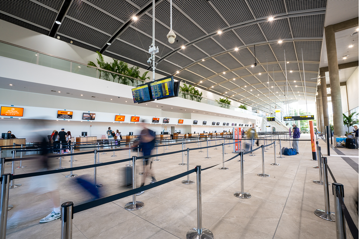 Cairns International T1 Airport. Modern airport terminal with check-in counters, digital displays, and passengers moving with luggage. Airport Interior Design Brisbane Australia