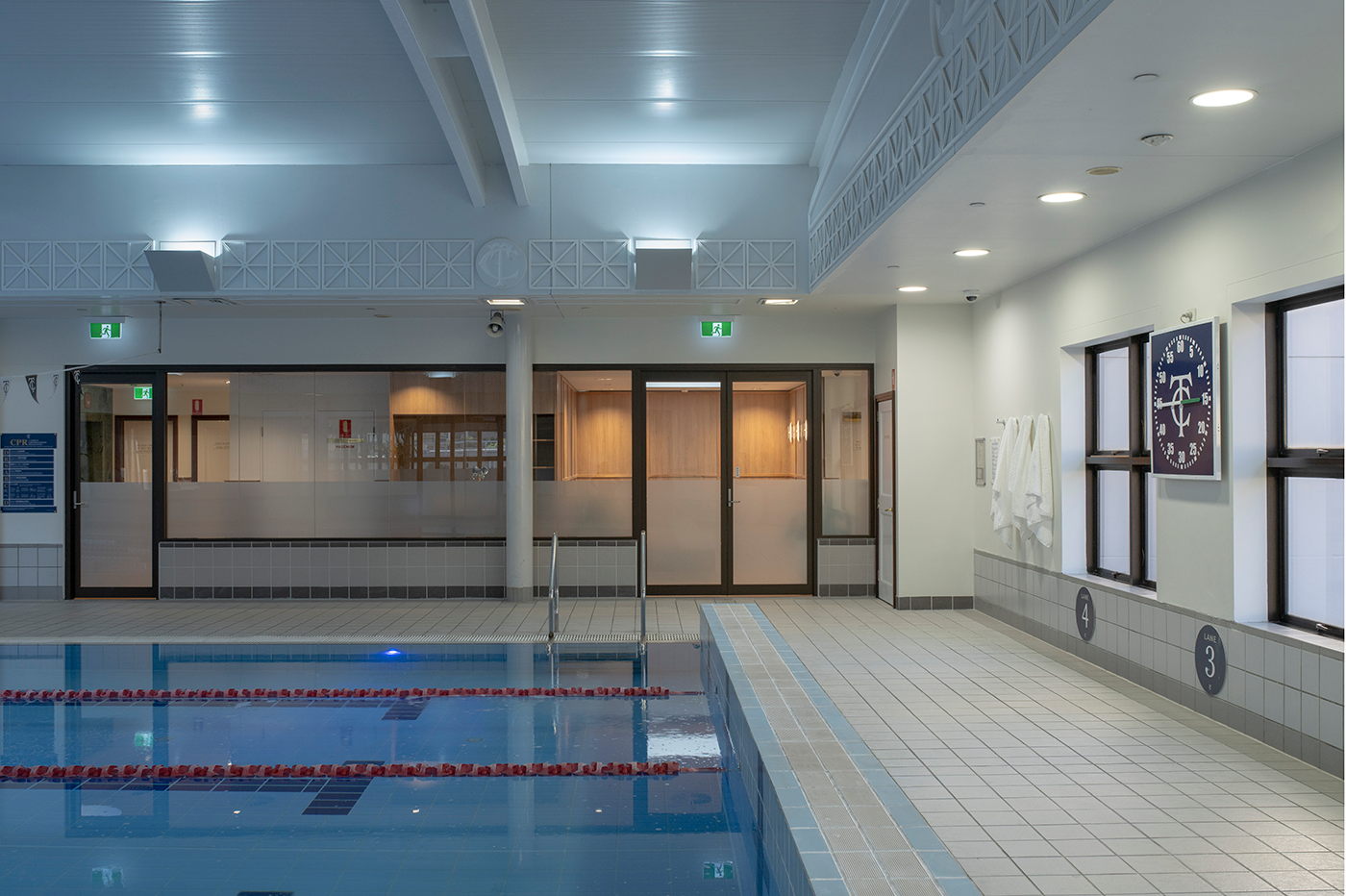 Tattersall's Club. Indoor swimming pool with lanes, poolside tiles, and a wall clock. Doors and changing room visible in the background. Hospitality Interior Design Brisbane Australia