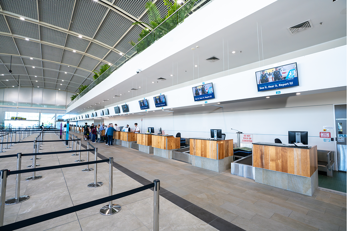 Airport check-in counters with wooden paneling and digital screens above, with passengers and staff present. Airport Interior Designers in Brisbane Australia