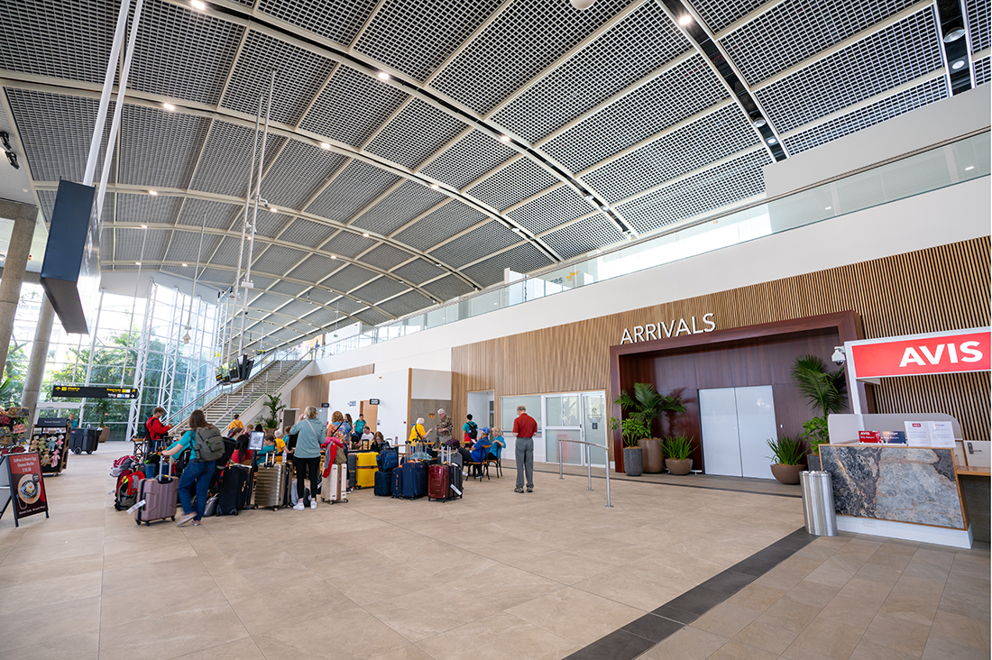 Cairns International T1 Airport. Airport arrivals area with passengers and luggage, "Arrivals" sign, and car rental desk. Airport Interior Design Brisbane Australia