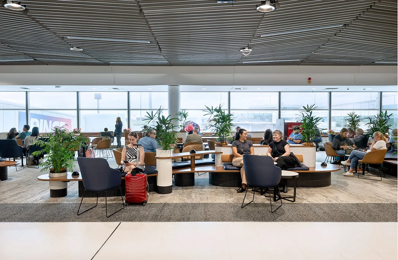 Modern airport lounge with travelers, seating areas, and large windows. Brisbane Airport Domestic Terminal. Retail Interior Design Australia