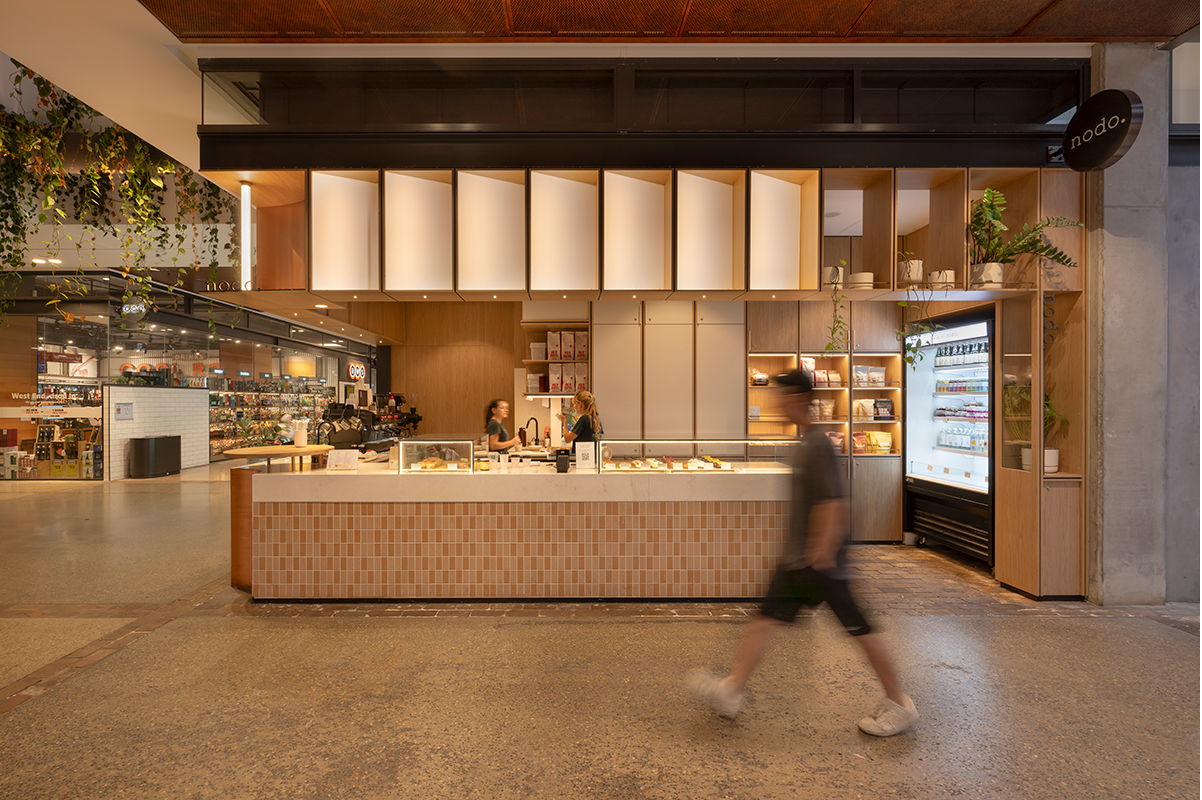 Modern cafe with counter and display fridge, blurred person walking by.