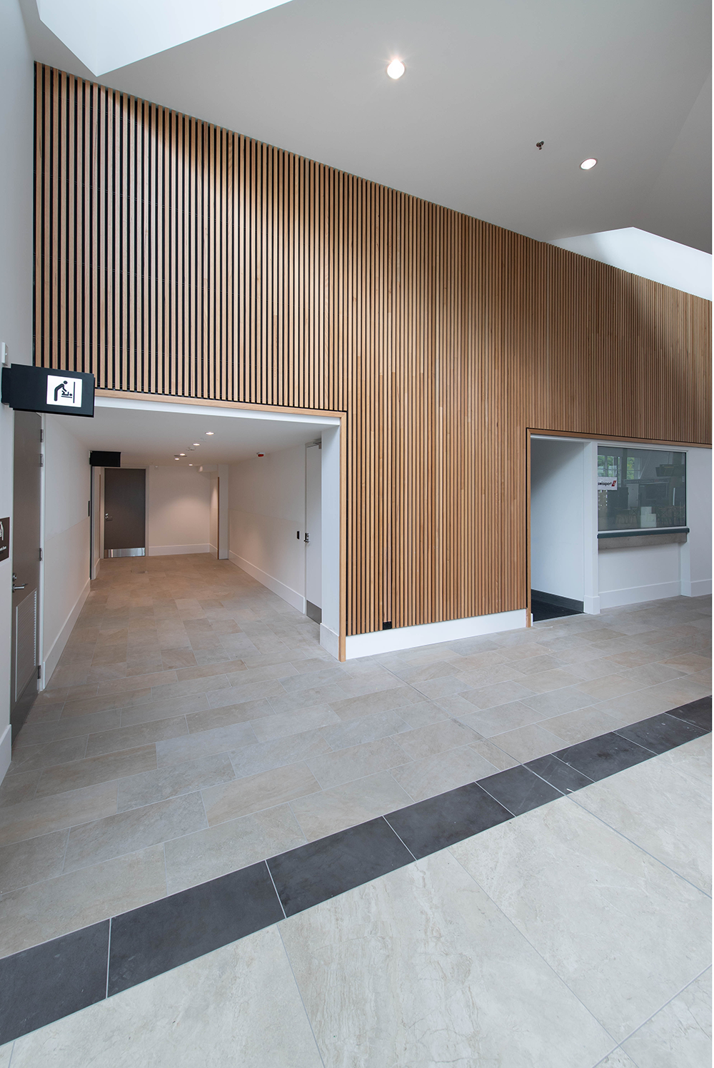 Cairns International T1 Airport. Modern interior hallway with wood paneling, tiled floor, and a wheelchair-accessible sign. Hospitality Interior Design Brisbane Australia