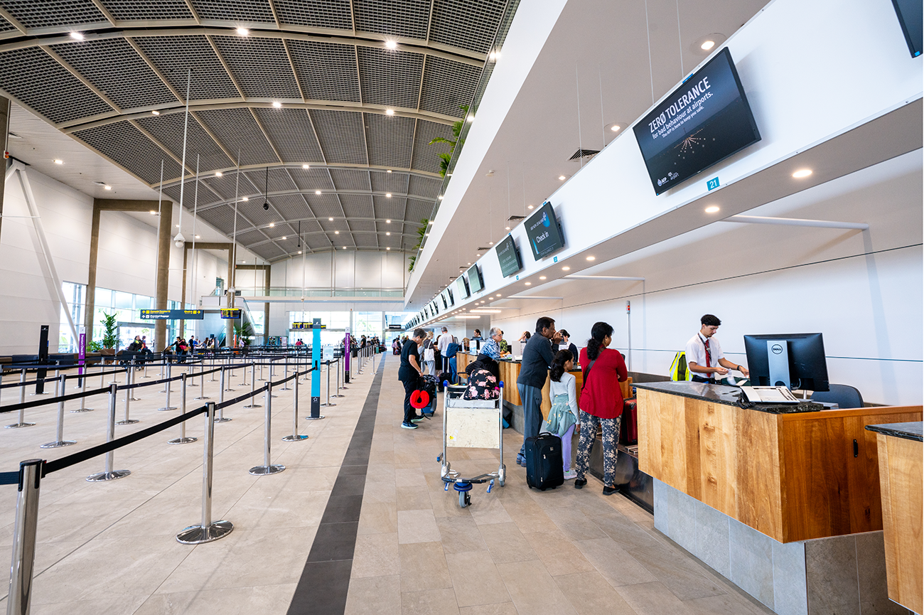 Cairns International T1 Airport. People checking in at a modern airport terminal with high ceilings, counters, and digital screens. Airport Interior Design Brisbane Australia