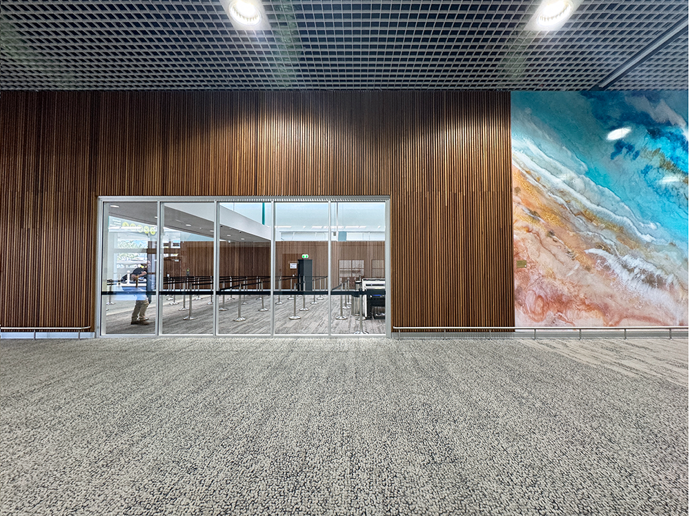 Interior of an airport with wood paneling, a large glass entrance, and abstract wall art.
Townsville Airport. Interior Design Australia