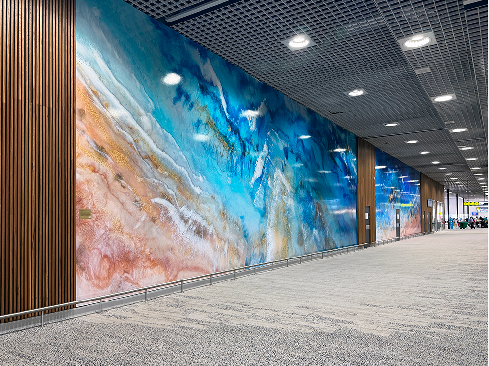 Large abstract mural in an airport hallway with vibrant blue and earthy hues, wooden panels, and ceiling lights.
Townsville Airport. Interior Design Australia