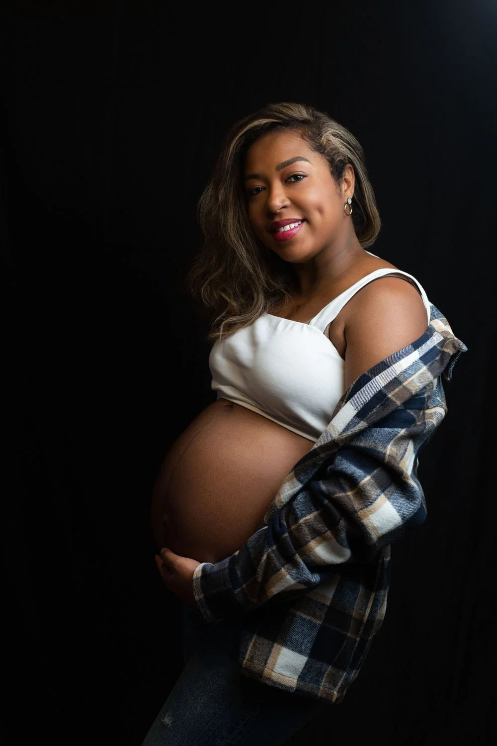 Pregnant Black woman with shirt falling off shoulder, and cradling bump smiles