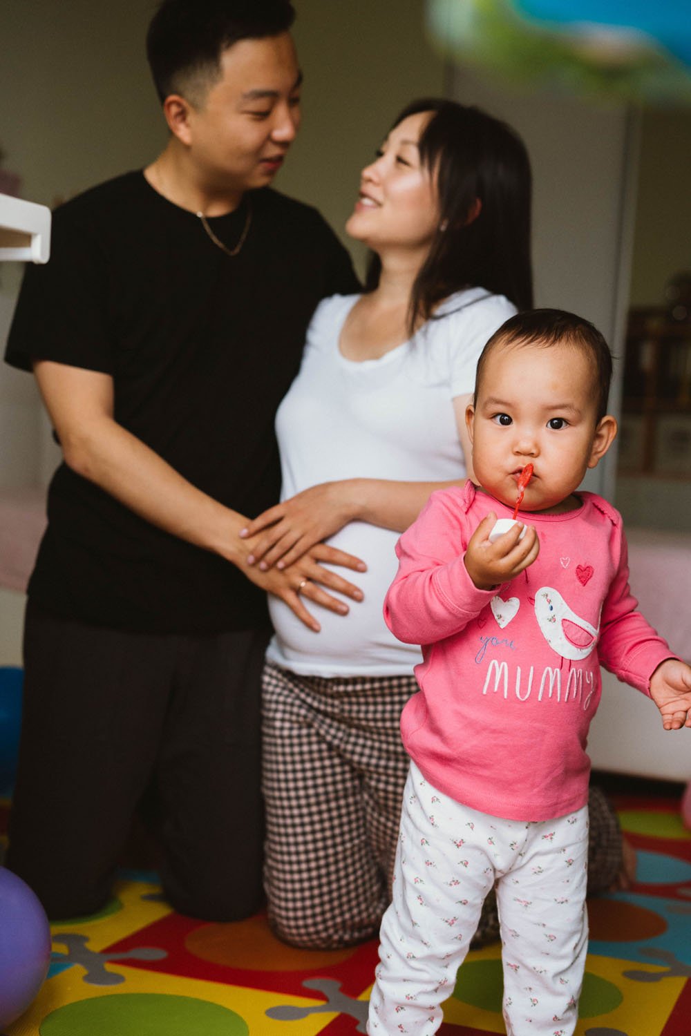 Father and mother with hands on bump during maternity photo shoot with toddler between them and the camera
