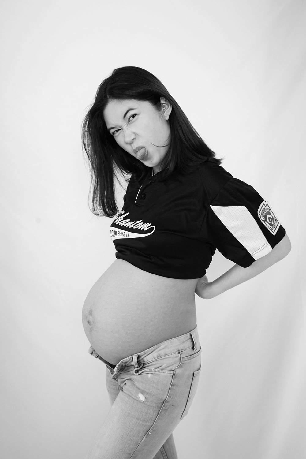 Cheeky tongue sticking out maternity photo of woman with jeans unbuttoned