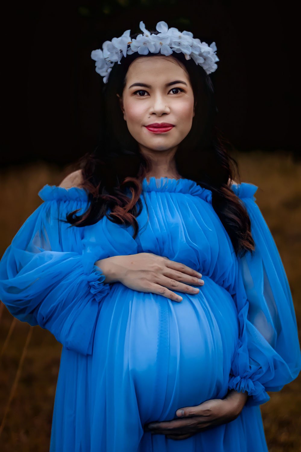 Pregnant Asian woman with flower garland smiles at the camera