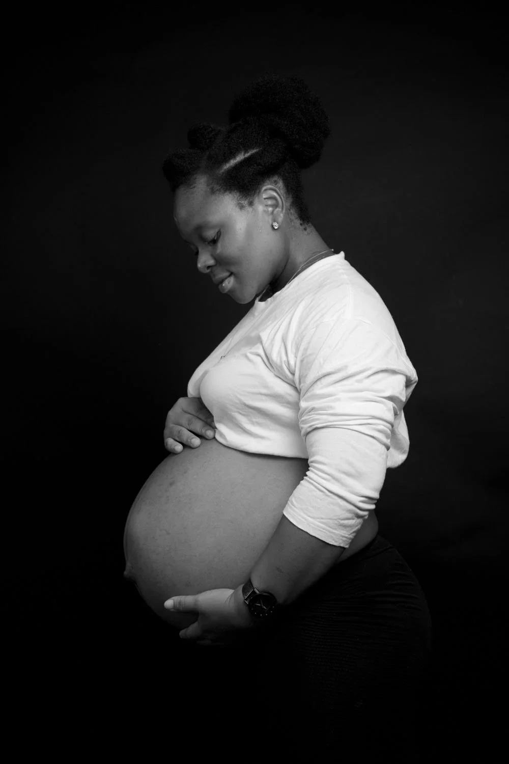 Portland Maternity photo of black woman cradling bump with black background