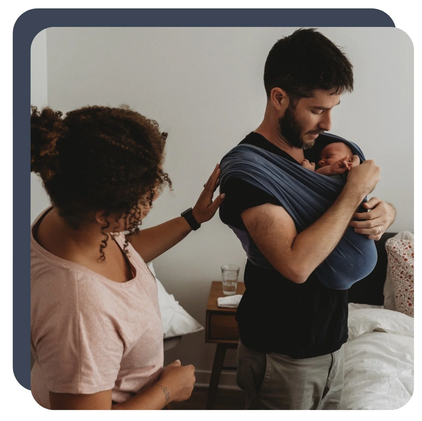A man holding a newborn baby close to his chest while a postpartum touches his shoulder.