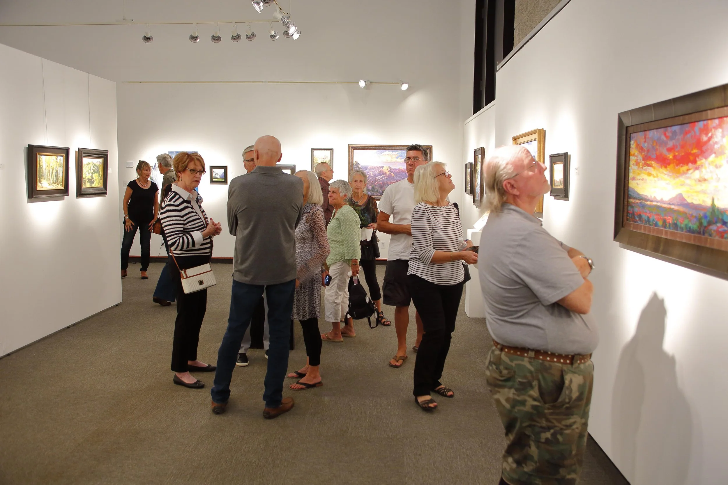 People viewing artwork in an art gallery with white walls and overhead lighting.