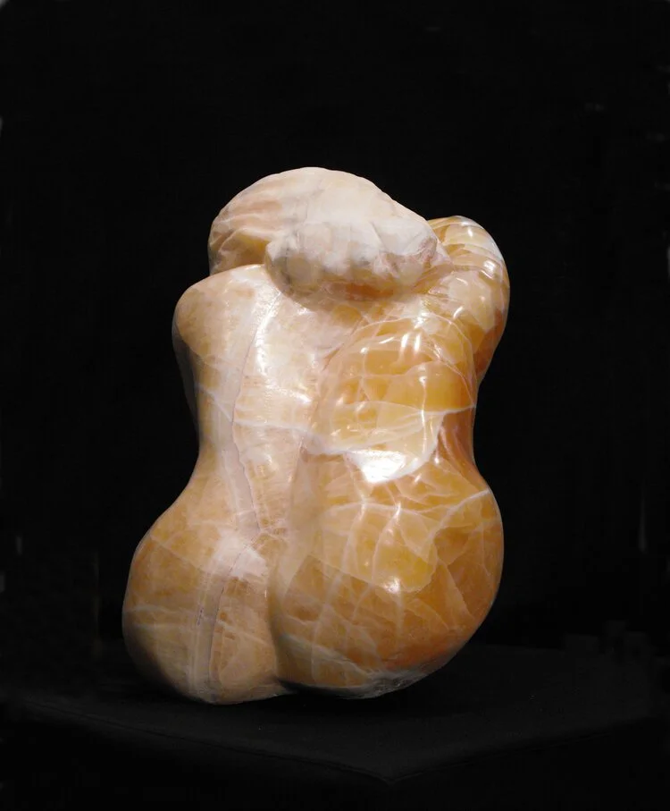 Onyx sculpture of a nude woman with a white head covering, created from orange and cream-colored onyx