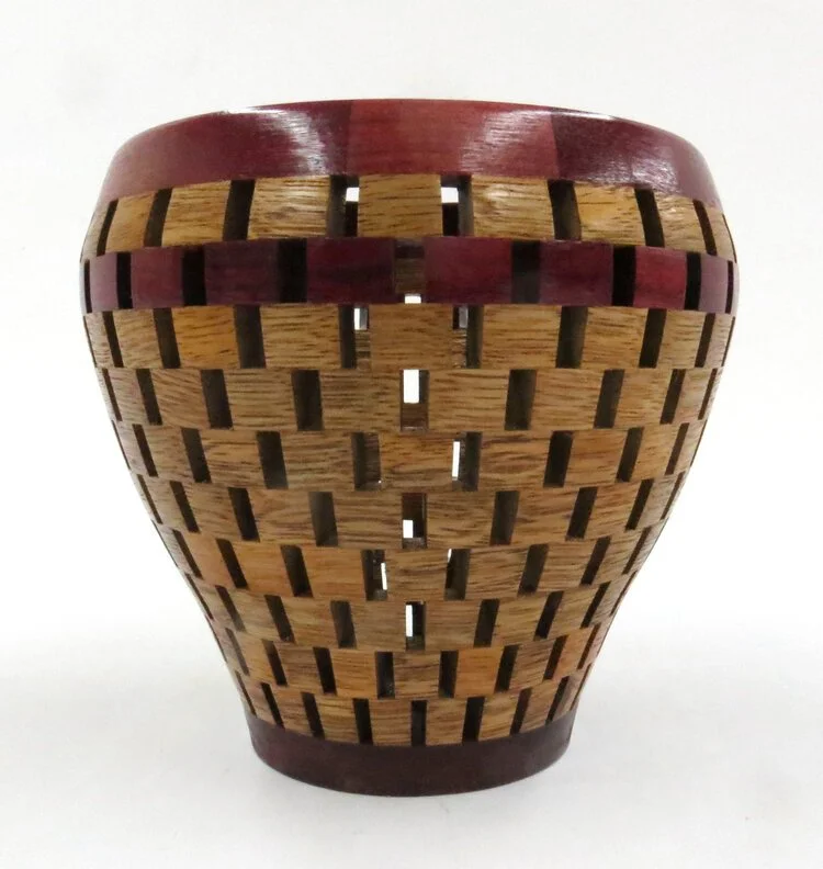 A wooden basket with a rounded shape, featuring a pattern of rectangular slats and a dark red rim at the top.