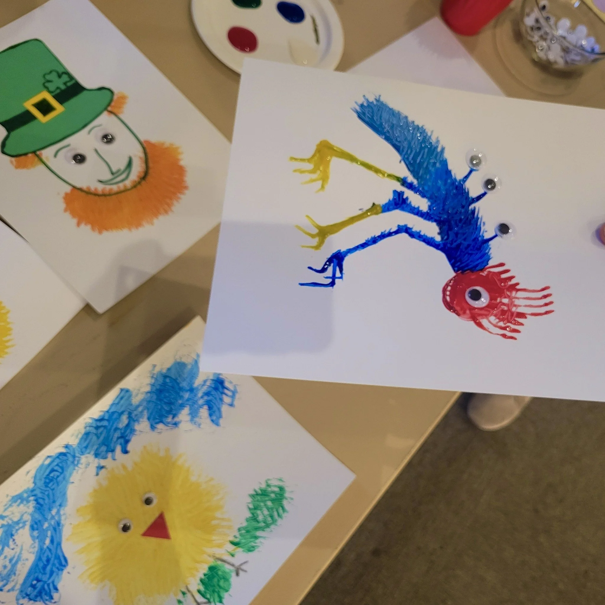 Colorful craft pictures of animals and a leprechaun, with googly eyes attached, created by children.