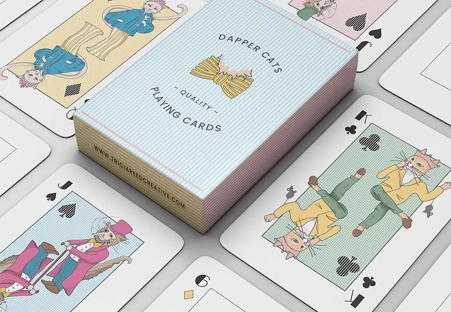 A deck of playing cards named 'Dapper Cats' with illustrated cats in various outfits on different cards, laid out on a table alongside other playing cards.