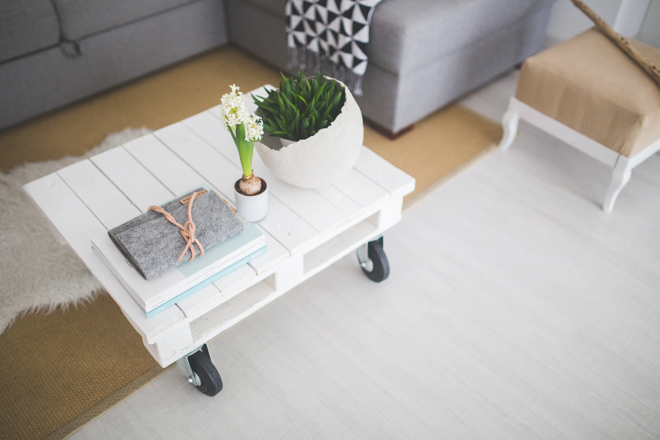 White coffee table with potted white hyacinth and green plant, placed on a beige rug, in front of a gray sofa and a beige upholstered chair in a cozy living room.