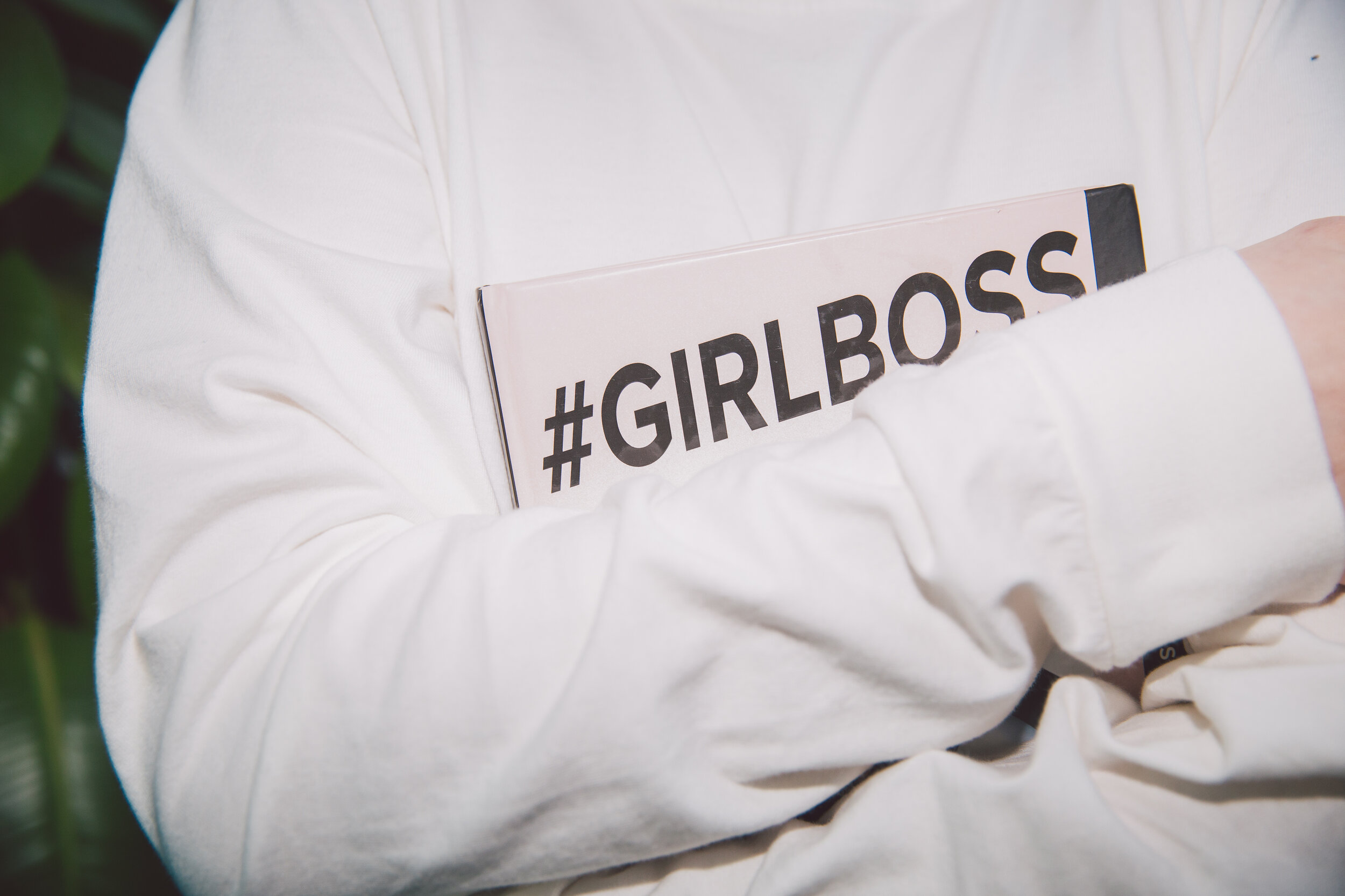 A person in a white shirt holding a book or magazine with the hashtag '#GIRLBOSS' on the cover.