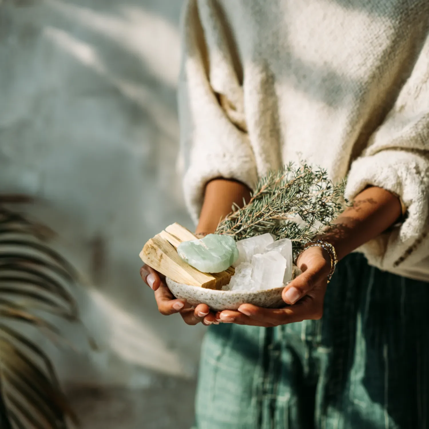Person holding a bowl with crystals, wooden piece, and greenery