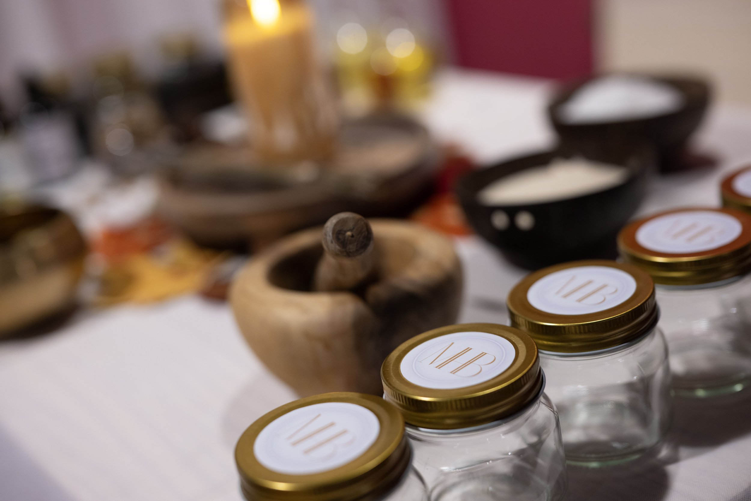 Close-up view of a table with various custom made branded bowls, jars, and a wooden mortar and pestle, some labeled jars with 'WIB' on the lids in the foreground, with blurred items in the background.