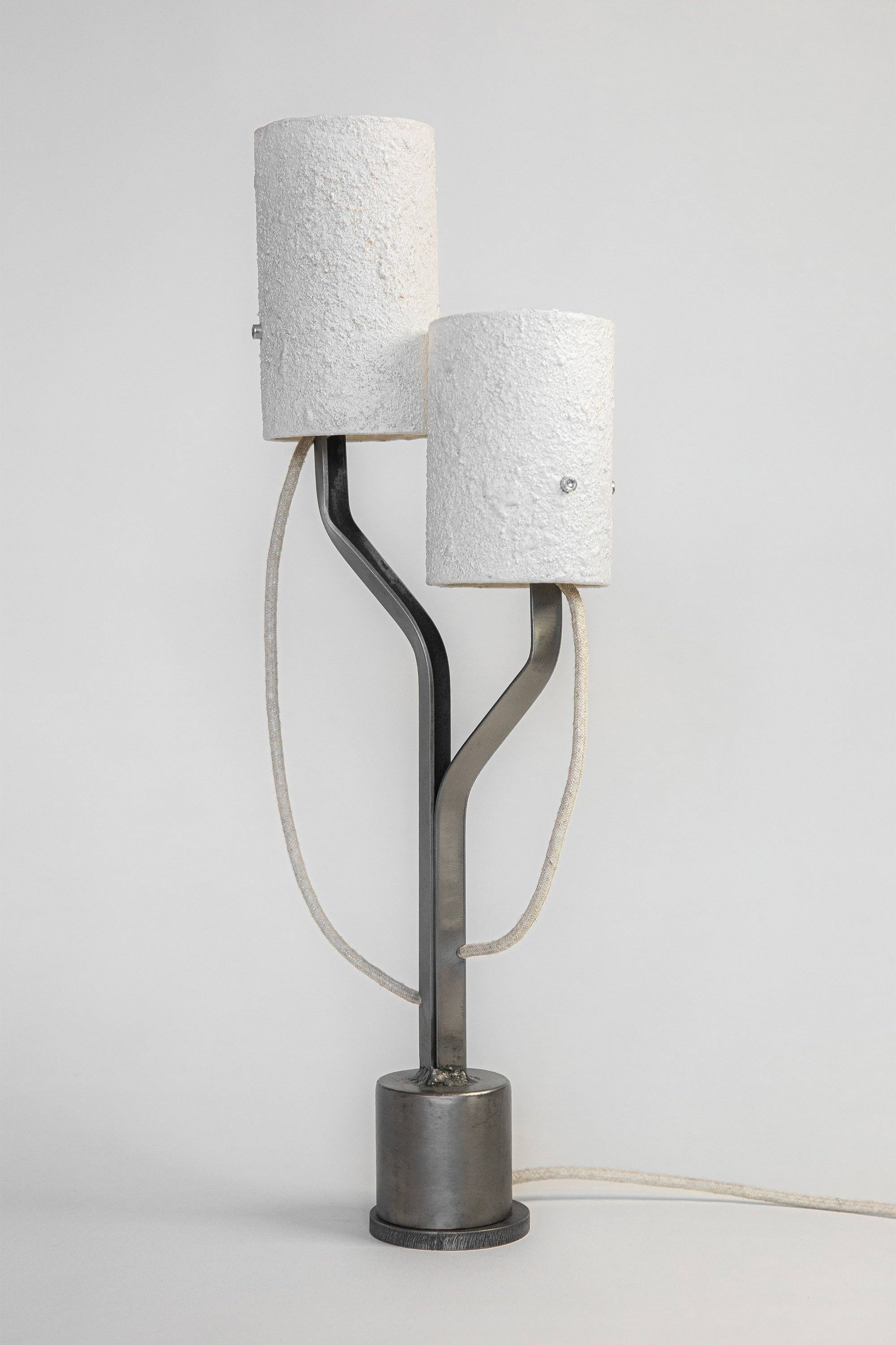 Modern lamp with textured stone-effect shades on a sleek frame. Curved branches extend from a cylindrical steel base, with textile cords wrapping around, blending style and function.