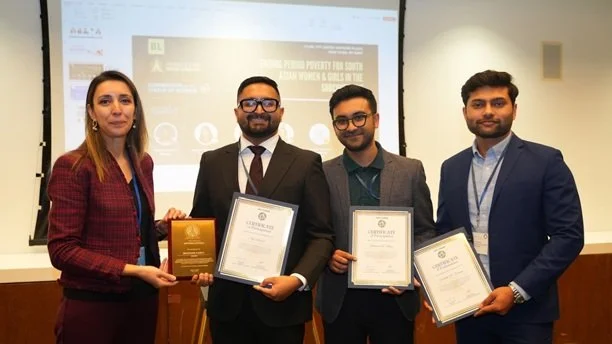 Four business professionals standing in front of a presentation screen, holding certificates and awards during a formal event or ceremony.