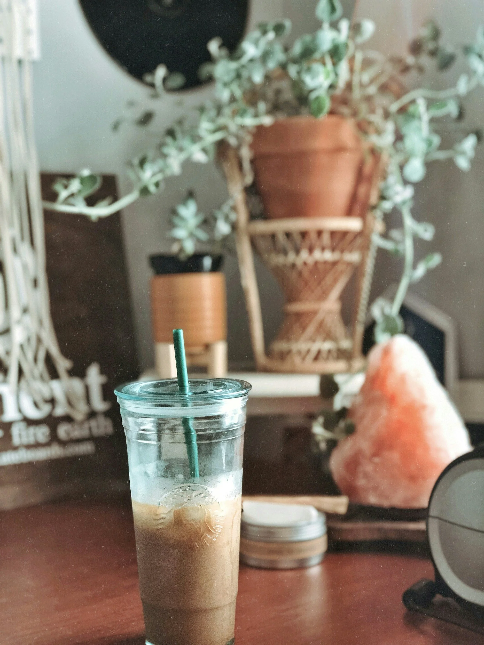 Image of iced coffee sitting on a desk with vibrant plants in the background