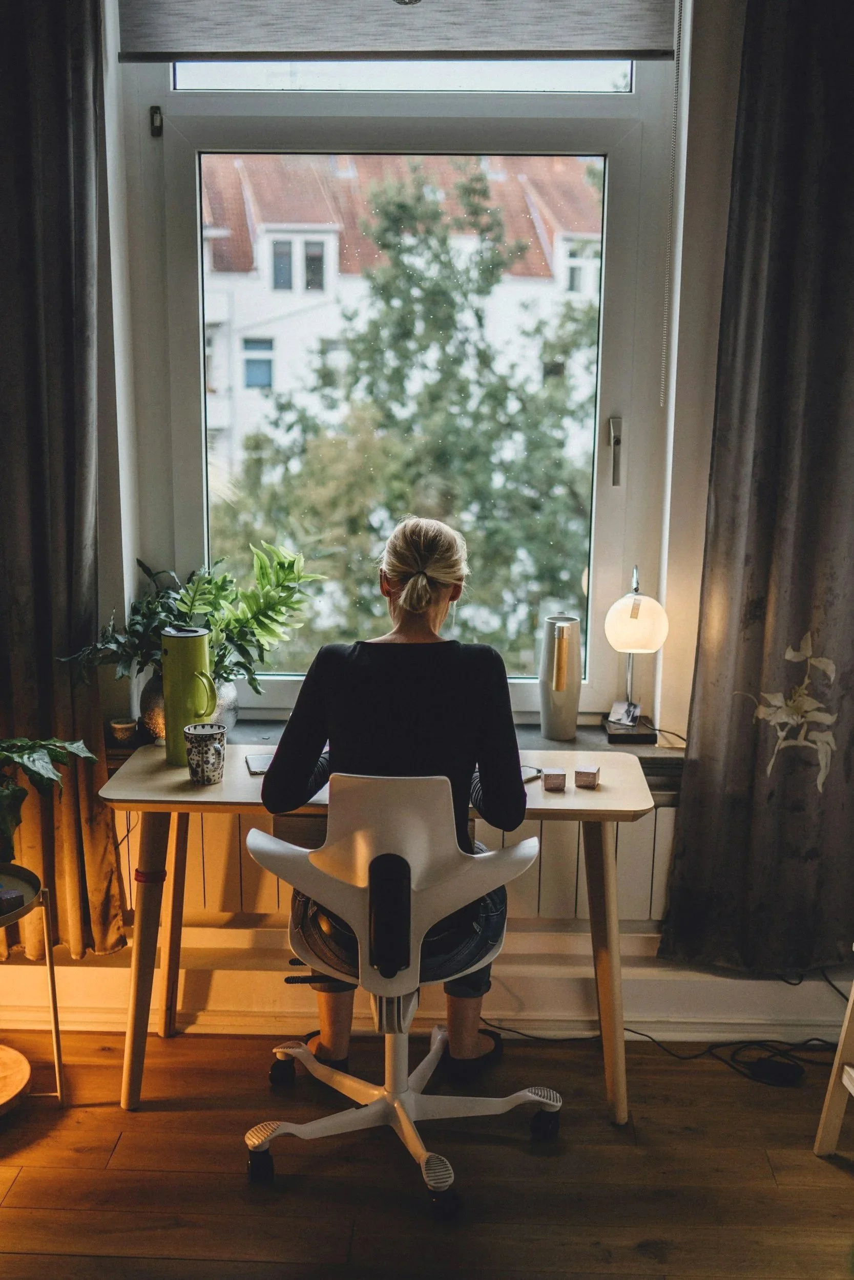 woman with blond hair sitting at a desk in front of a window