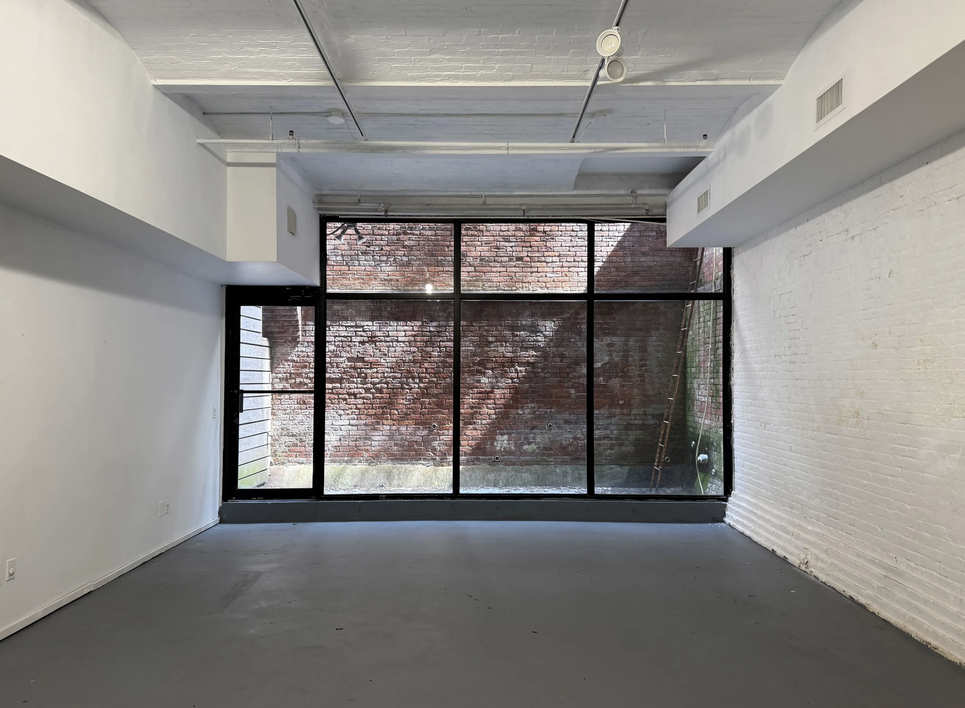 Empty room with large glass window looking out onto a brick wall, with ladder leaning against the wall outside.