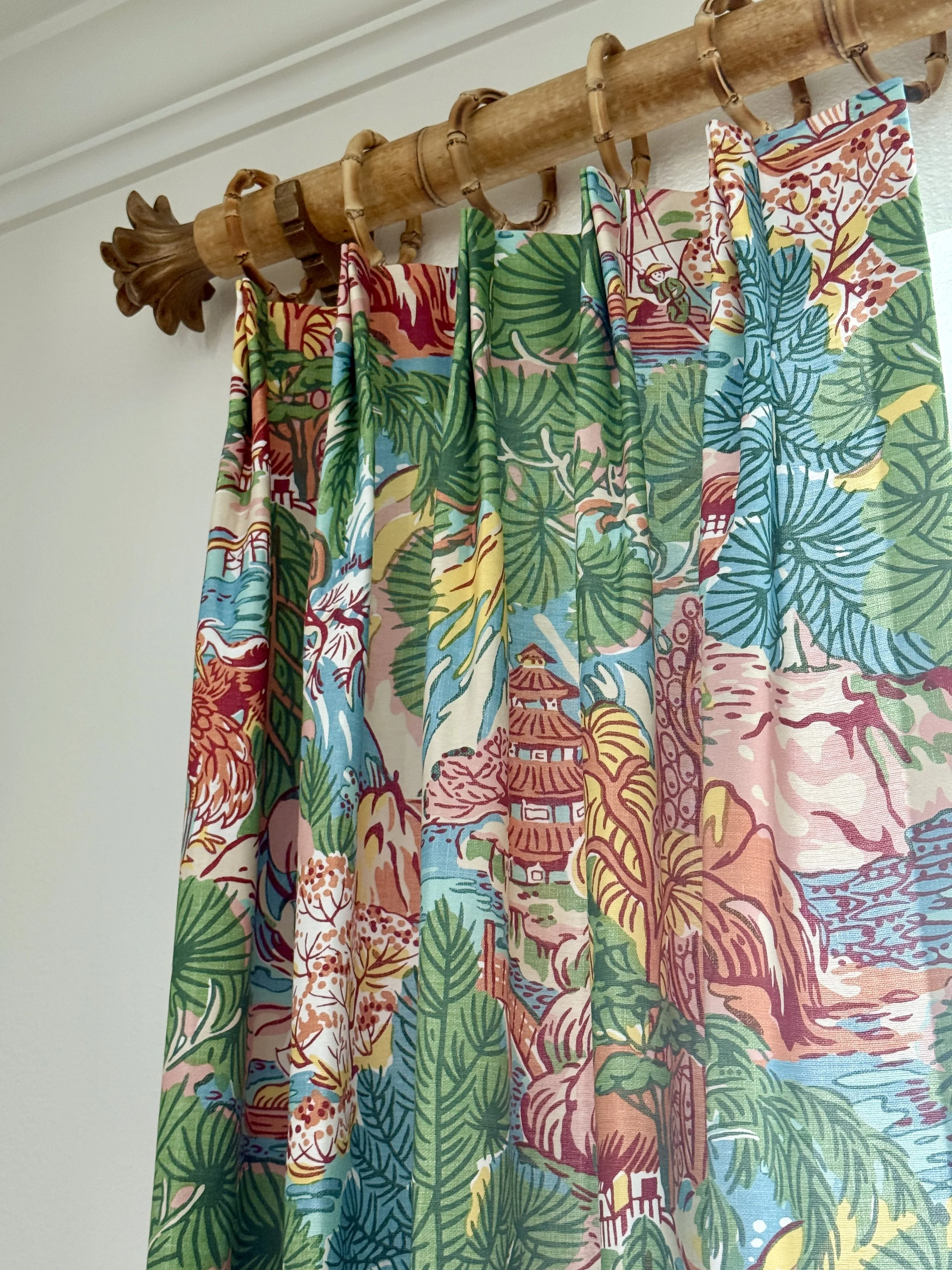 Colorful curtains hanging on a rod against a blue wall, with one coral-colored curtain on the left and a patterned curtain with gold embroidery on the right.