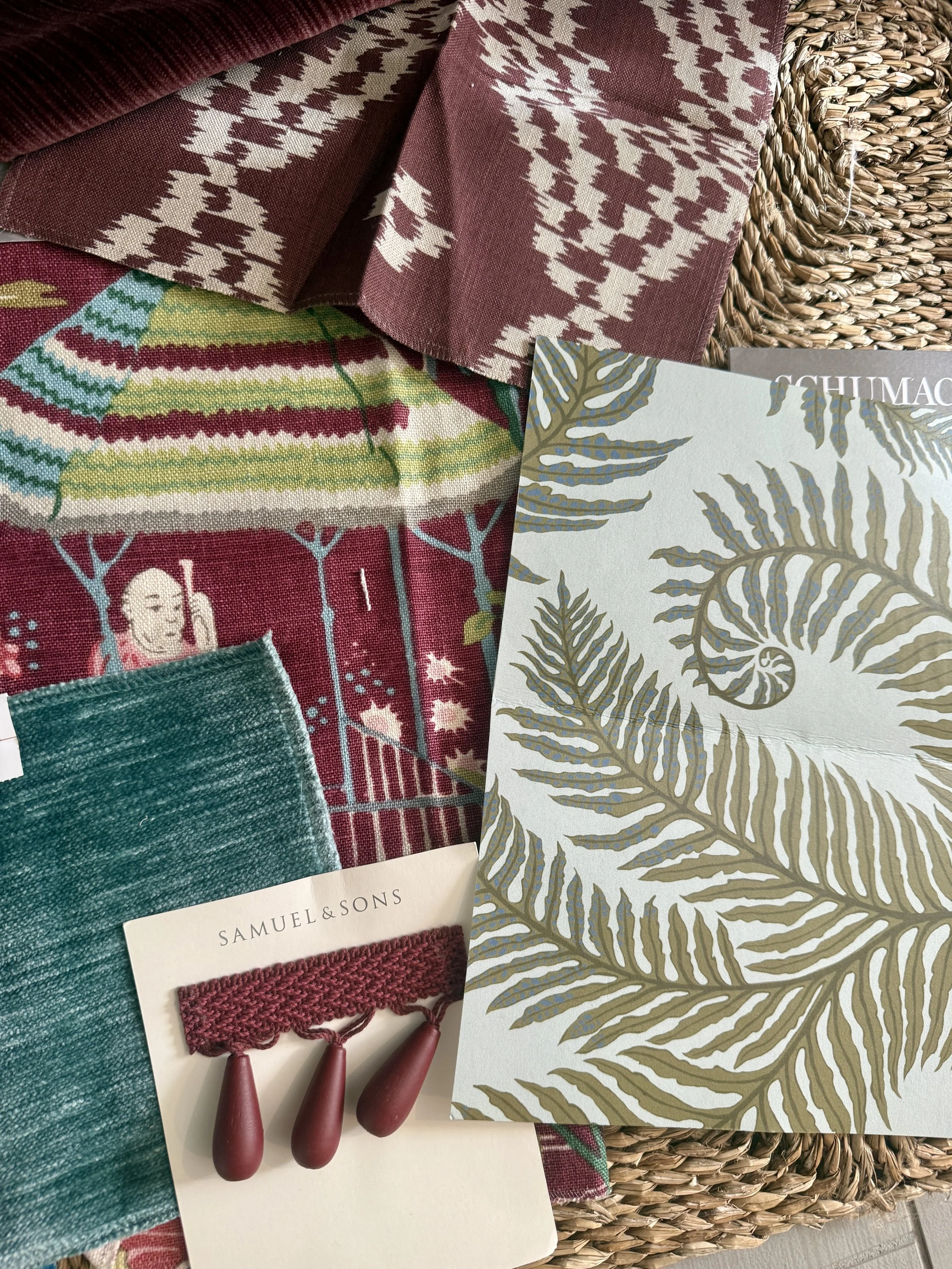 Three patterned fabric swatches layered on a wooden surface. The top swatch is green and white with a scalloped design. The middle swatch features black outlines of pink, orange, and green berries and leaves on a white background. The bottom swatch is plain purple.