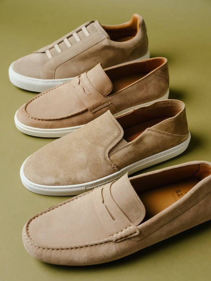 Four beige shoes, including sneakers, loafers, and slip-ons, arranged on a green background.