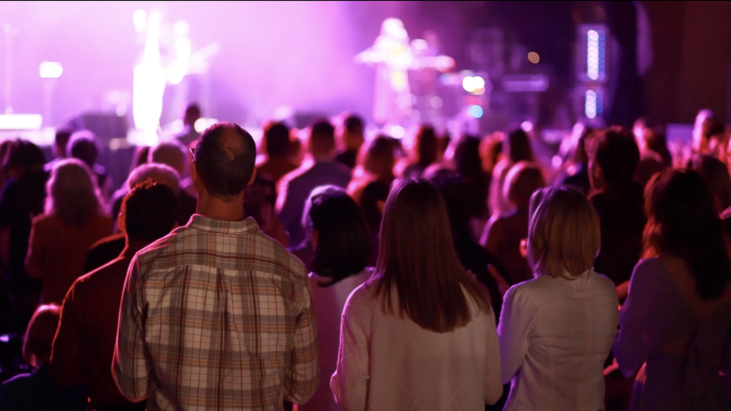 An audience watching a live performance under purple stage lights