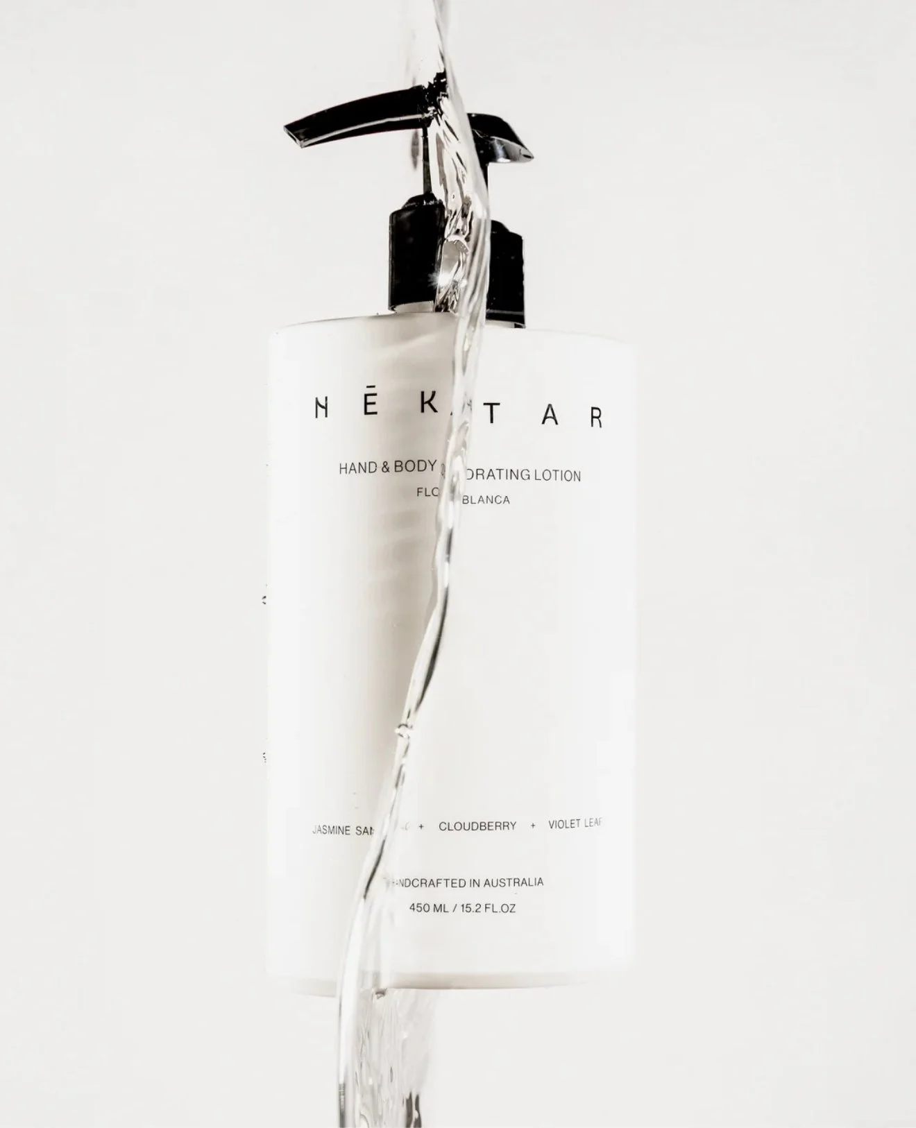 A white bottle with a black pump dispenser and black text, with water pouring over it.