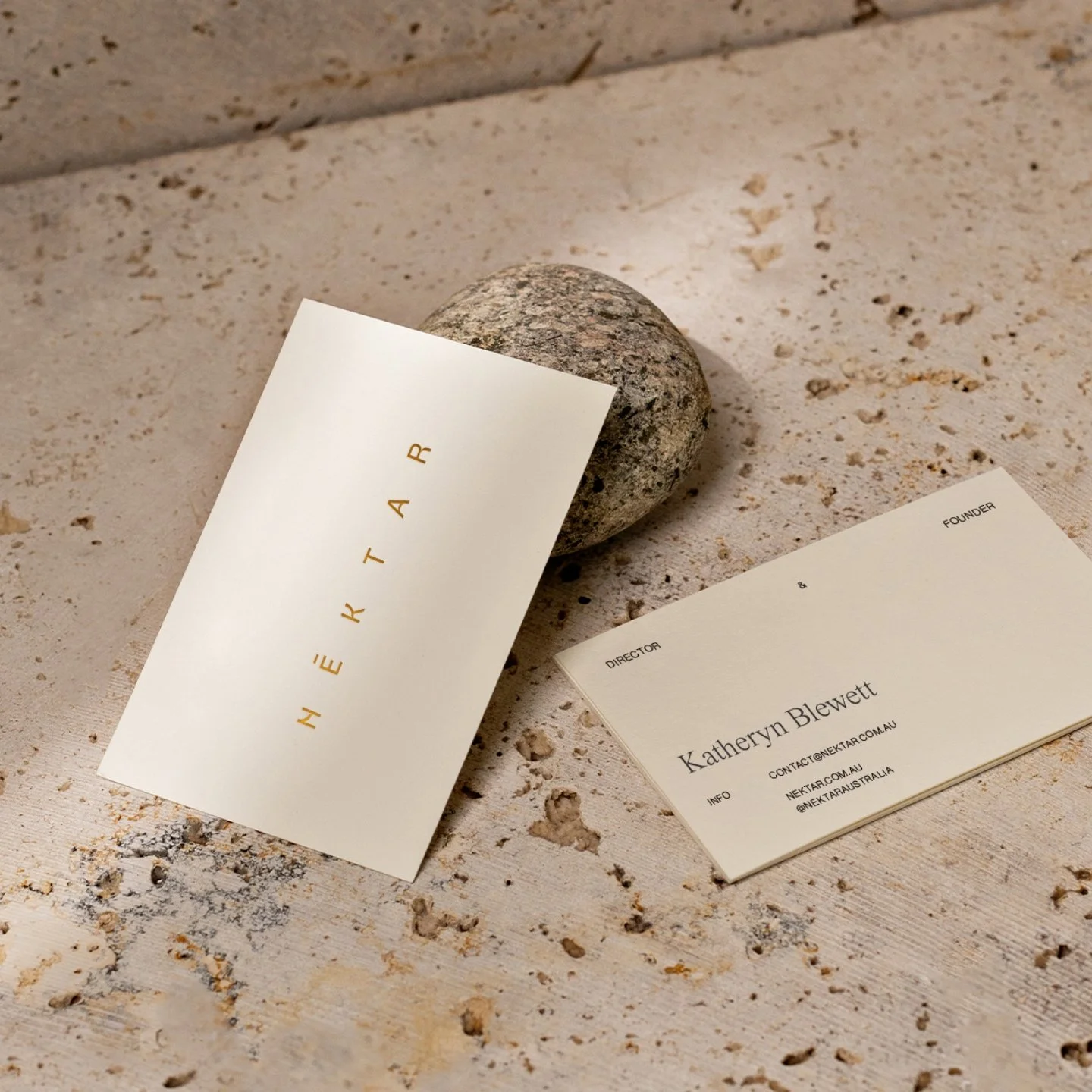 Two business cards, one with the name Heather, and the other with the name Katheryn Blewett, are resting on a textured surface next to a smooth oval stone.