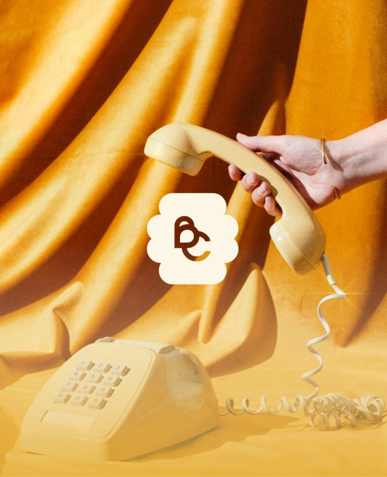 A person holding a yellow rotary phone in front of a yellow fabric backdrop.