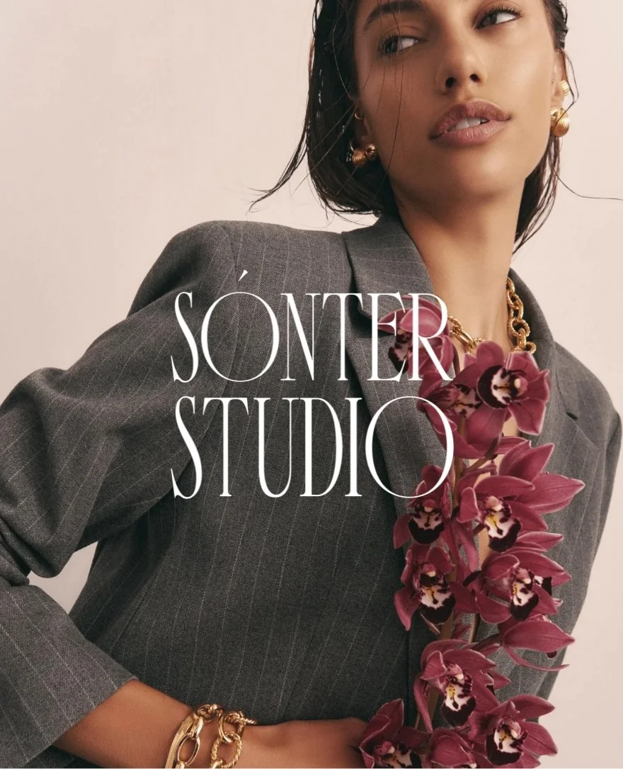 A woman wearing a dark gray pinstripe blazer with large gold jewelry, holding a deep pink orchid flower. The image features the text 'SÓNTER STUDIO' overlaid.