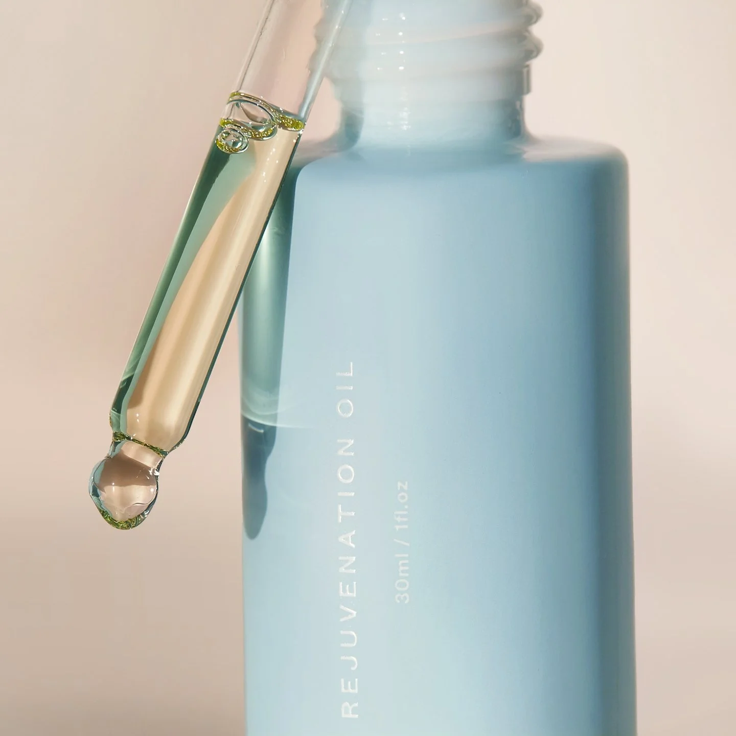 A light blue bottle labeled 'REJUVENATION OIL' with a clear dropper containing a transparent liquid, against a plain background.
