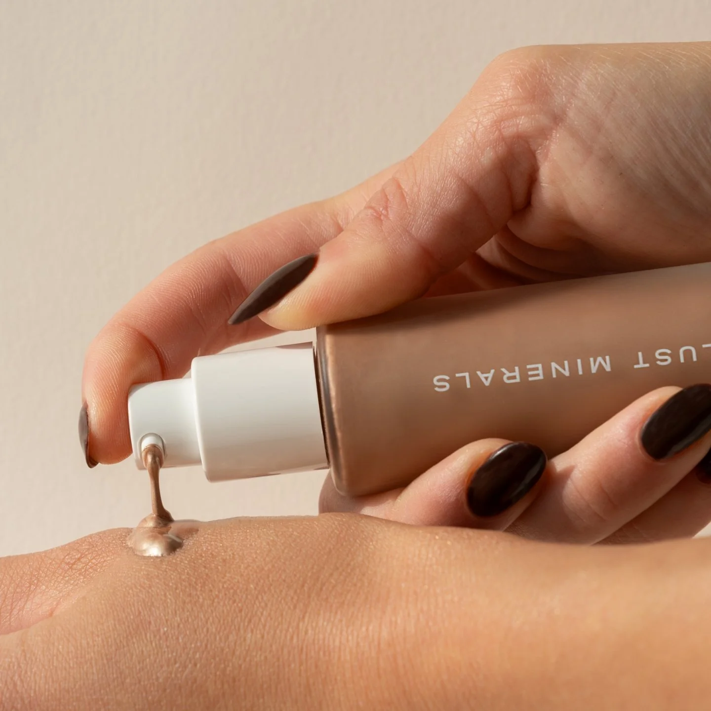 Close-up of a hand with dark nail polish squeezing beige foundation from a tube labeled 'LIFT MINERAL' onto the back of another hand.