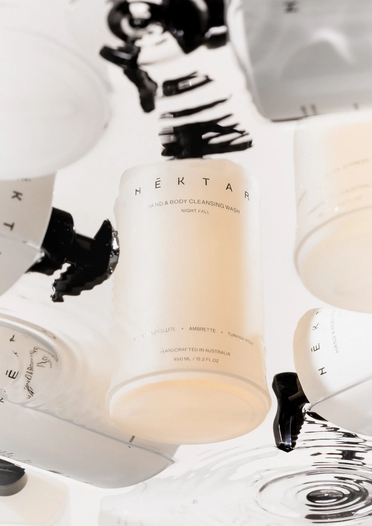 A collection of white bottles with black caps and black text, with one bottle in focus that says ‘NEKTAR’ and ‘HAND & BODY CLEANSING WASH NIGHT FALL’.